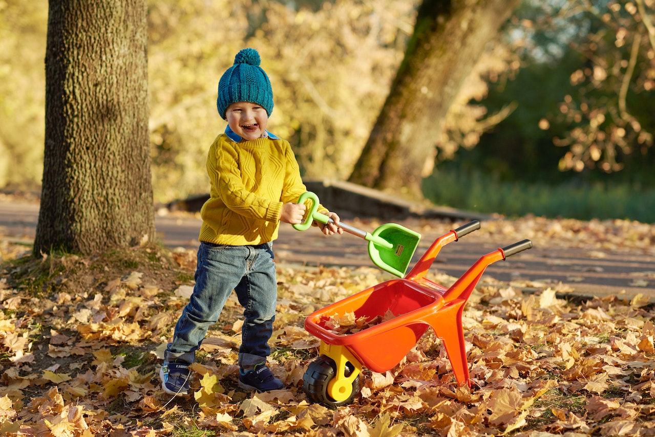 Dziecko bawi się jesiennymi liśćmi ubrany w odpowiednią odzież jesienną